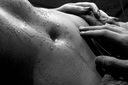 Photo noir et blanc du ventre d'une femme perlé de transpiration carressé d'une main