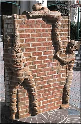 Photo d'un oeuvre d'art avec un mur de brique sur lequel sont scultés des gens qui l'escalade