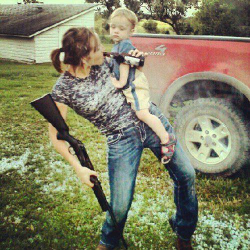 Photo d'une femme qui boit une bière, tient un fusil et son enfant