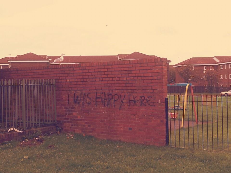 Photo d'un mur de brique rouge taggé "I was happy here"